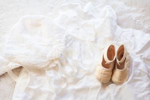 White baptismal gown and small cream-colored shoes laid out on white fabric.