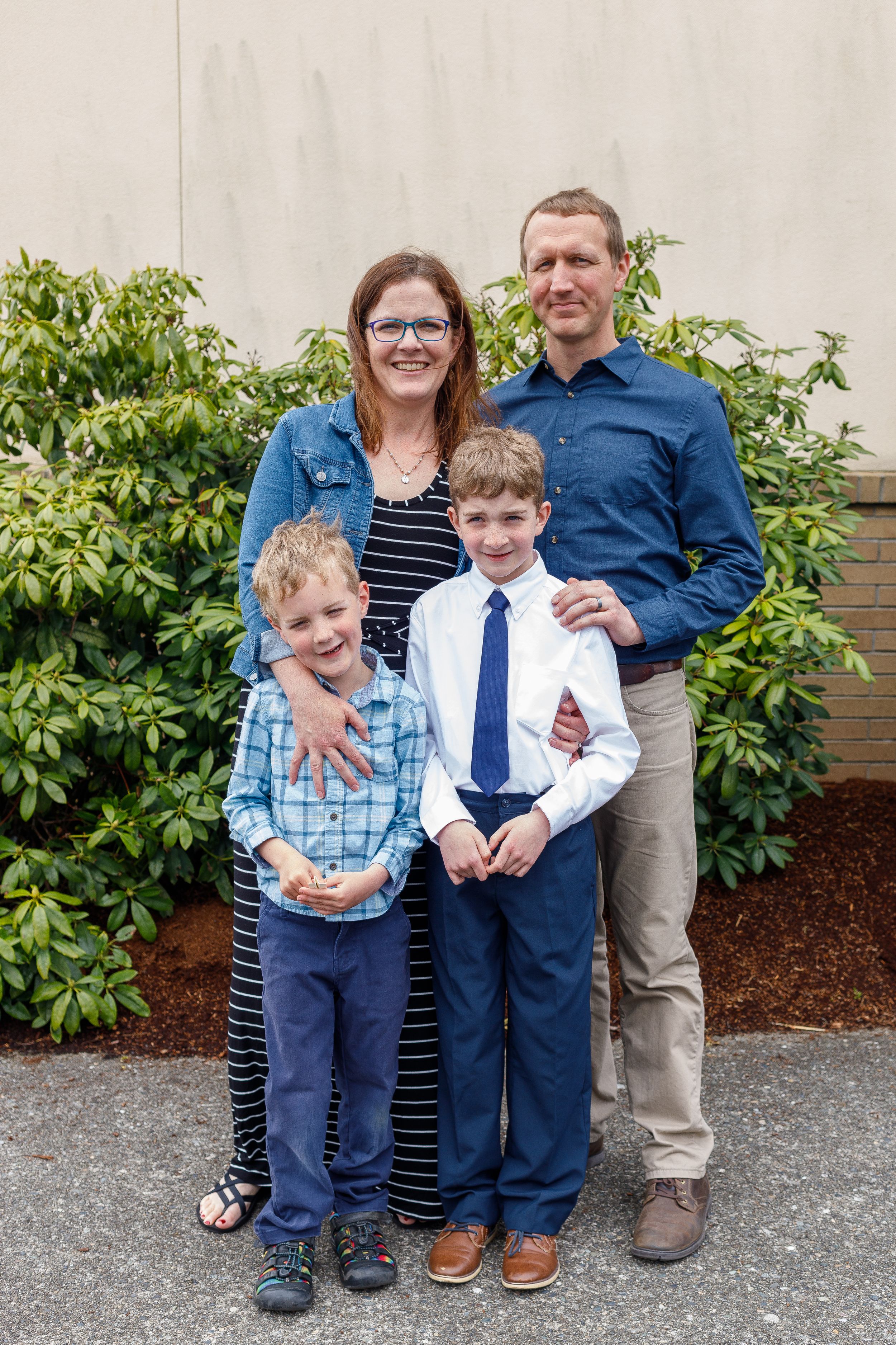 A family poses together in front of greenery wearing coordinated blue and navy outfits.