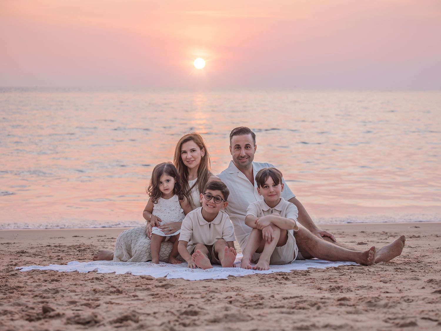 Familj sitter på stranden i solnedgång, Familjefotografering Västerås, MemoriebyM