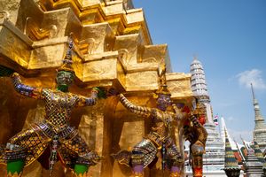 Golden temple architecture with traditional Thai decorative elements under blue sky.