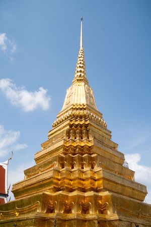 Golden stupa spire detail with ornate Thai architectural elements against blue sky.