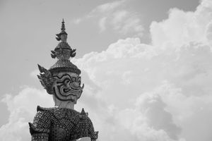 Ornate Thai temple guardian statues against cloudy sky in black and white.