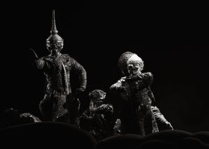 Dark theatrical scene with ornate figures illuminated against black background.