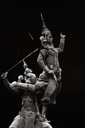 Traditional Thai masked dance performance in dramatic black and white lighting on stage.