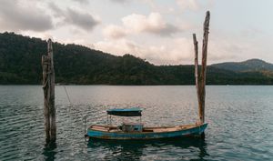 Wooden poles stand in calm water with a small boat visible in the distance.