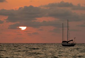 Orange sunset over ocean horizon with silhouettes of boats against the sky.