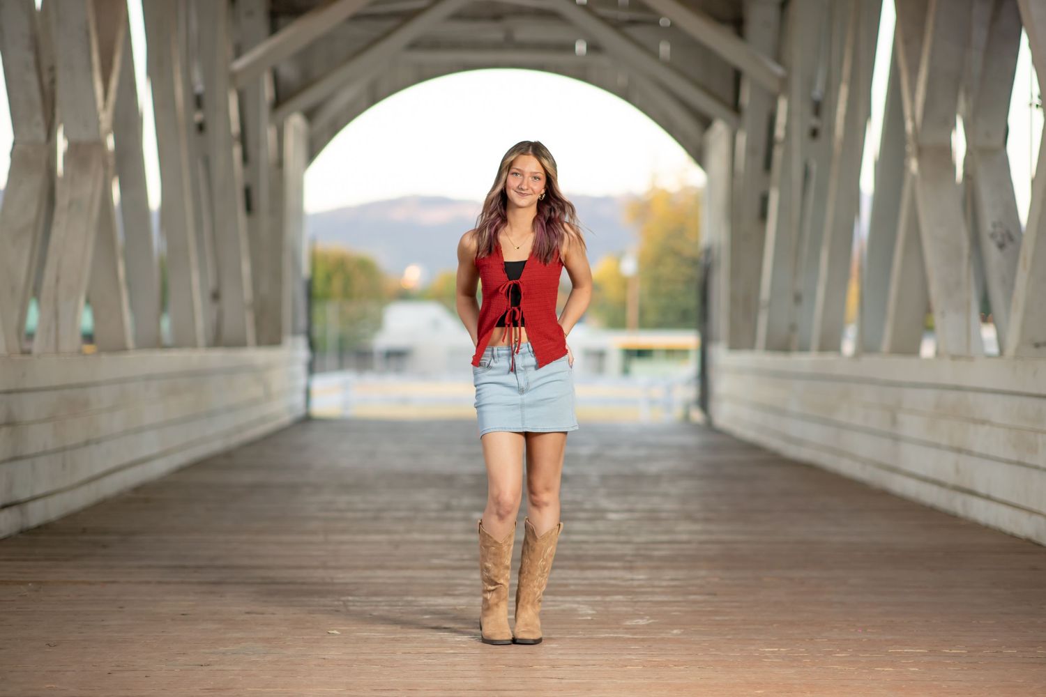 A casually dressed woman in a light jacket and jeans poses against a white building exterior.