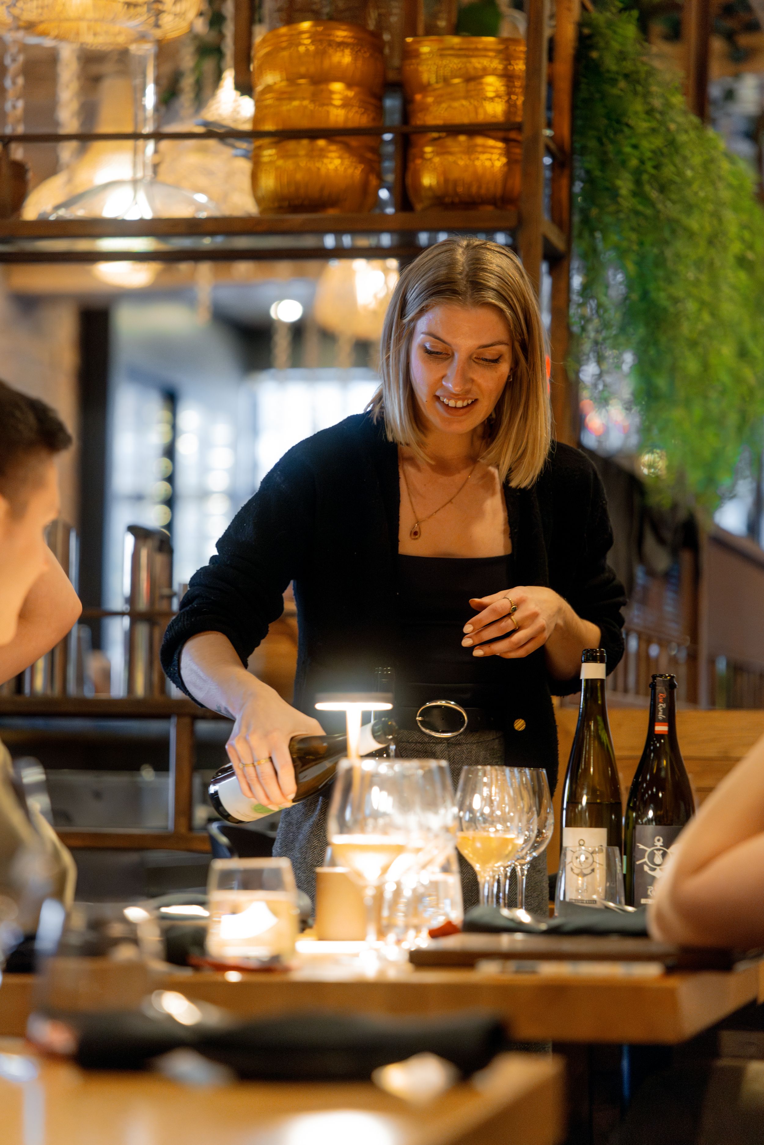 Restaurant service in progress with wine being poured at a warmly lit dining table.