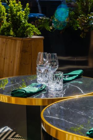 Empty wine glasses and emerald green napkins set on a dark marble table with gold trim under outdoor lighting.