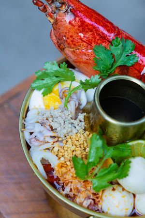 Khao tom seafood rice bowl topped with lobster, eggs, and fresh herbs being assembled in sequential steps.