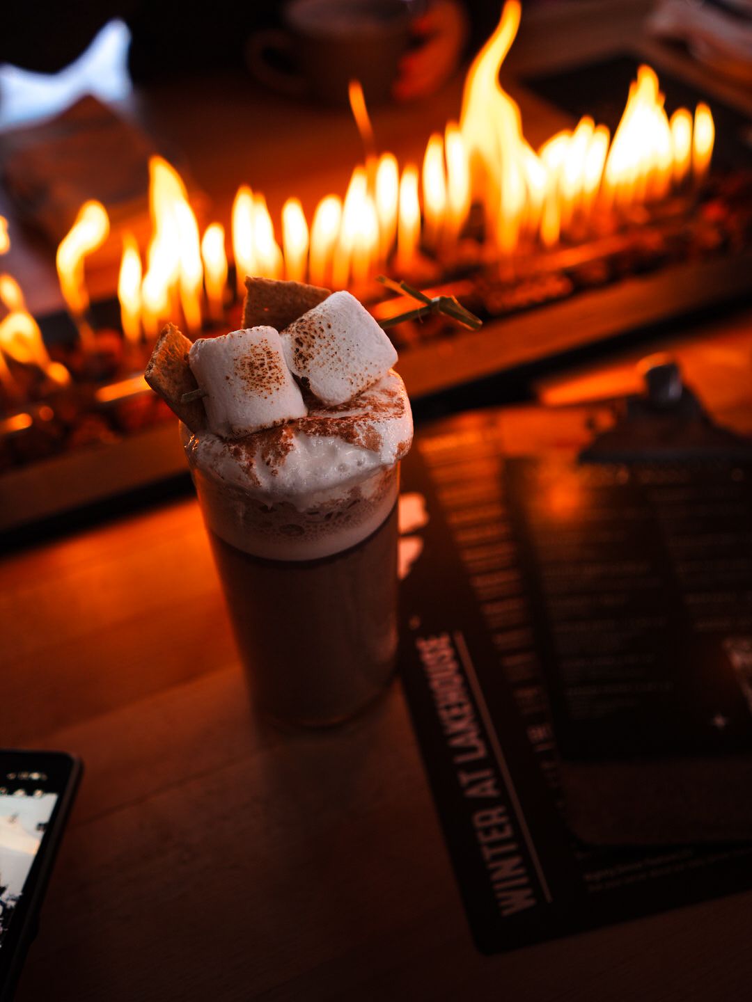 Hot chocolate drinks with whipped cream served beside glowing candles.