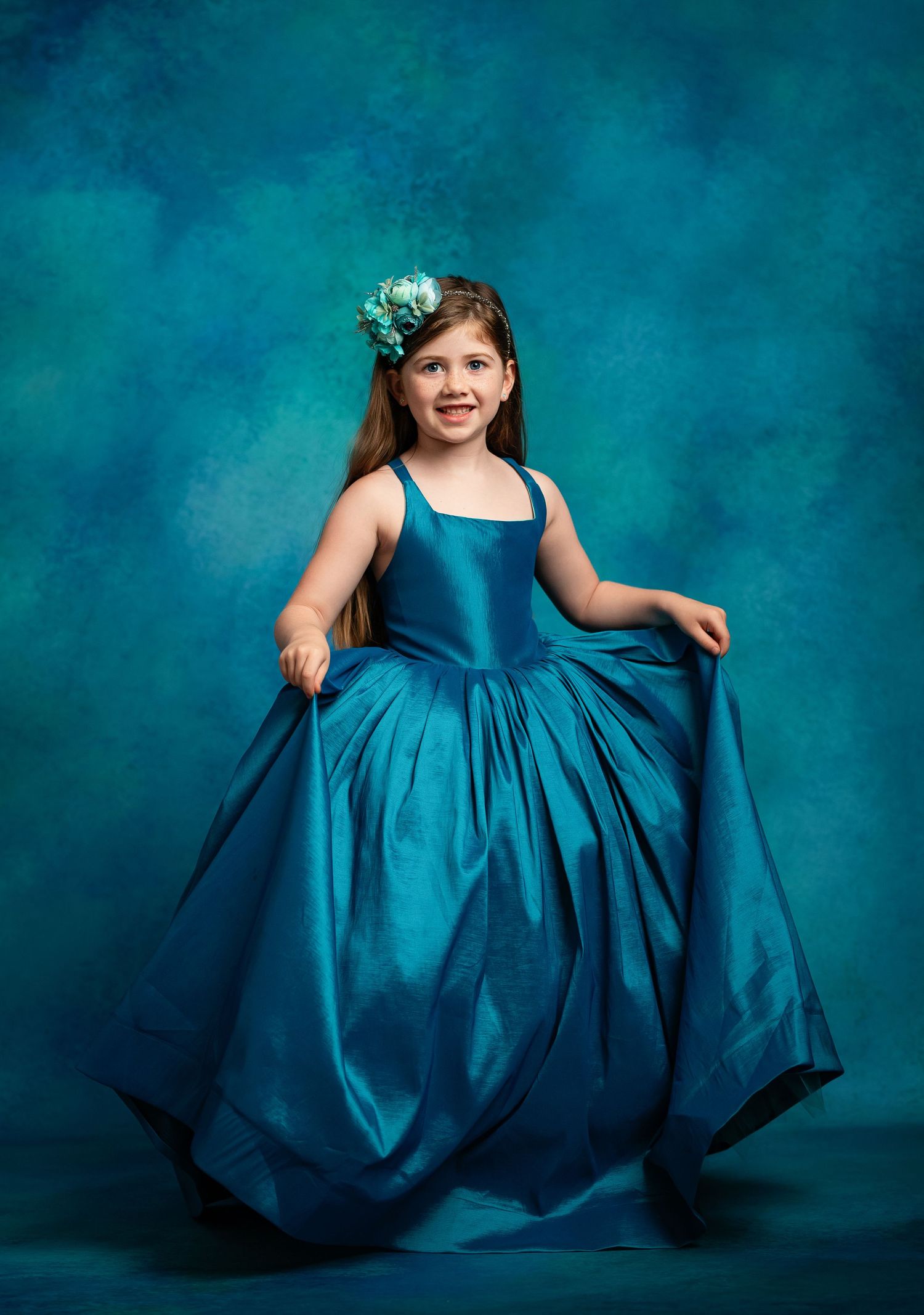 Elegant portrait featuring a ruffled turquoise ball gown against matching blue backdrop.