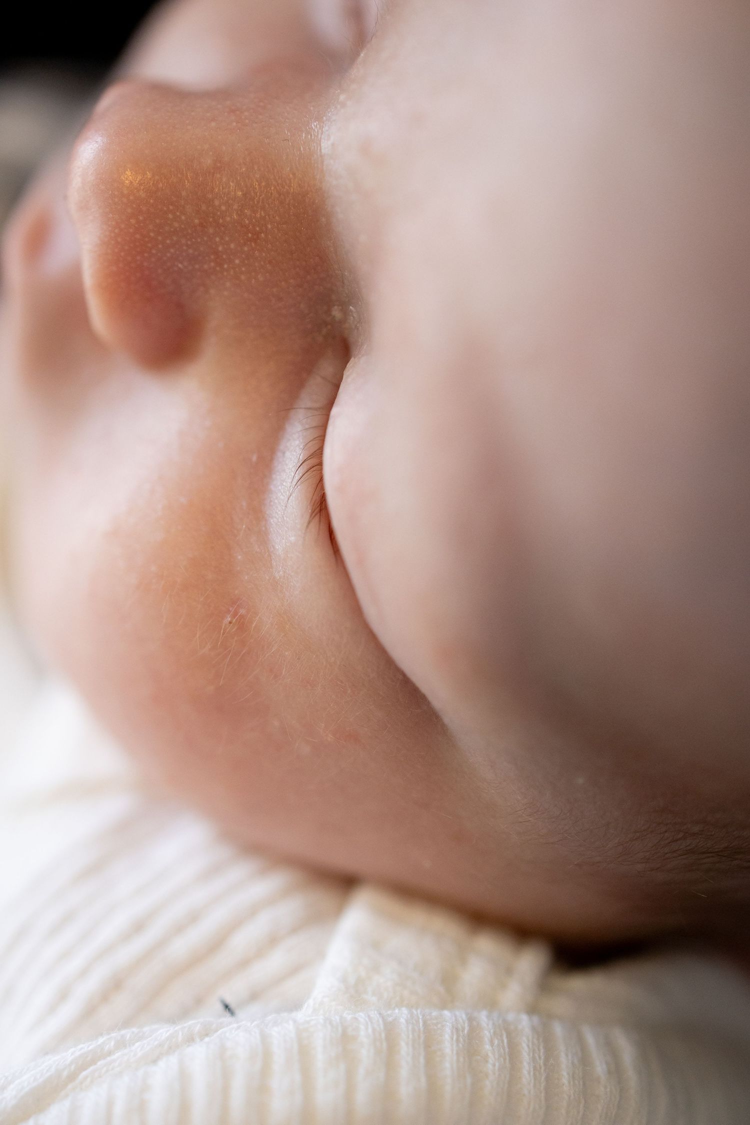 Close-up of a sleeping baby's chubby cheeks and chin, wearing a cream knit outfit, with soft natural lighting.
