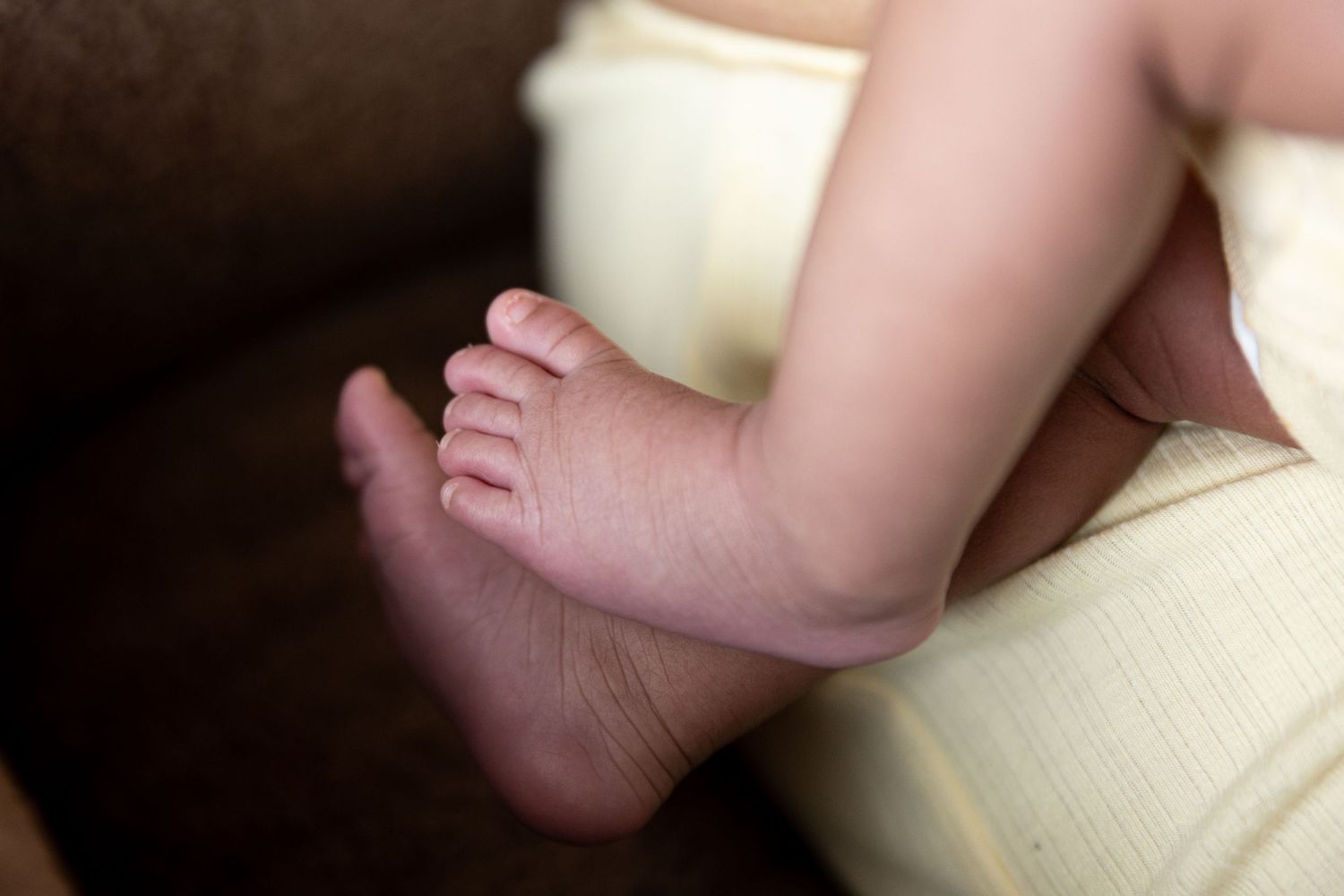 Close-up of adorable chubby newborn baby feet resting on a soft yellow blanket.