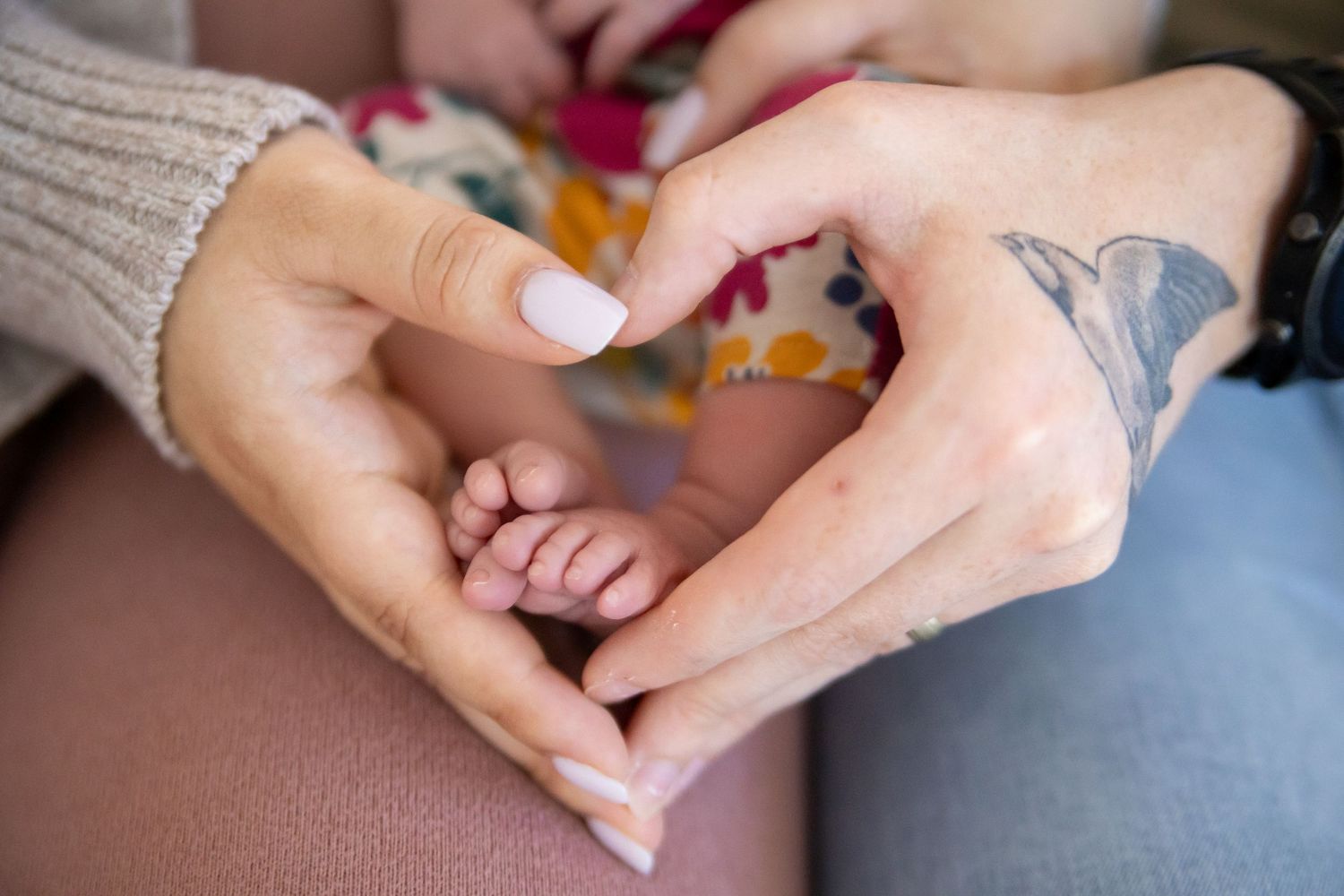 Hands gently form a heart shape holding a tiny baby foot while wearing a cream sweater.