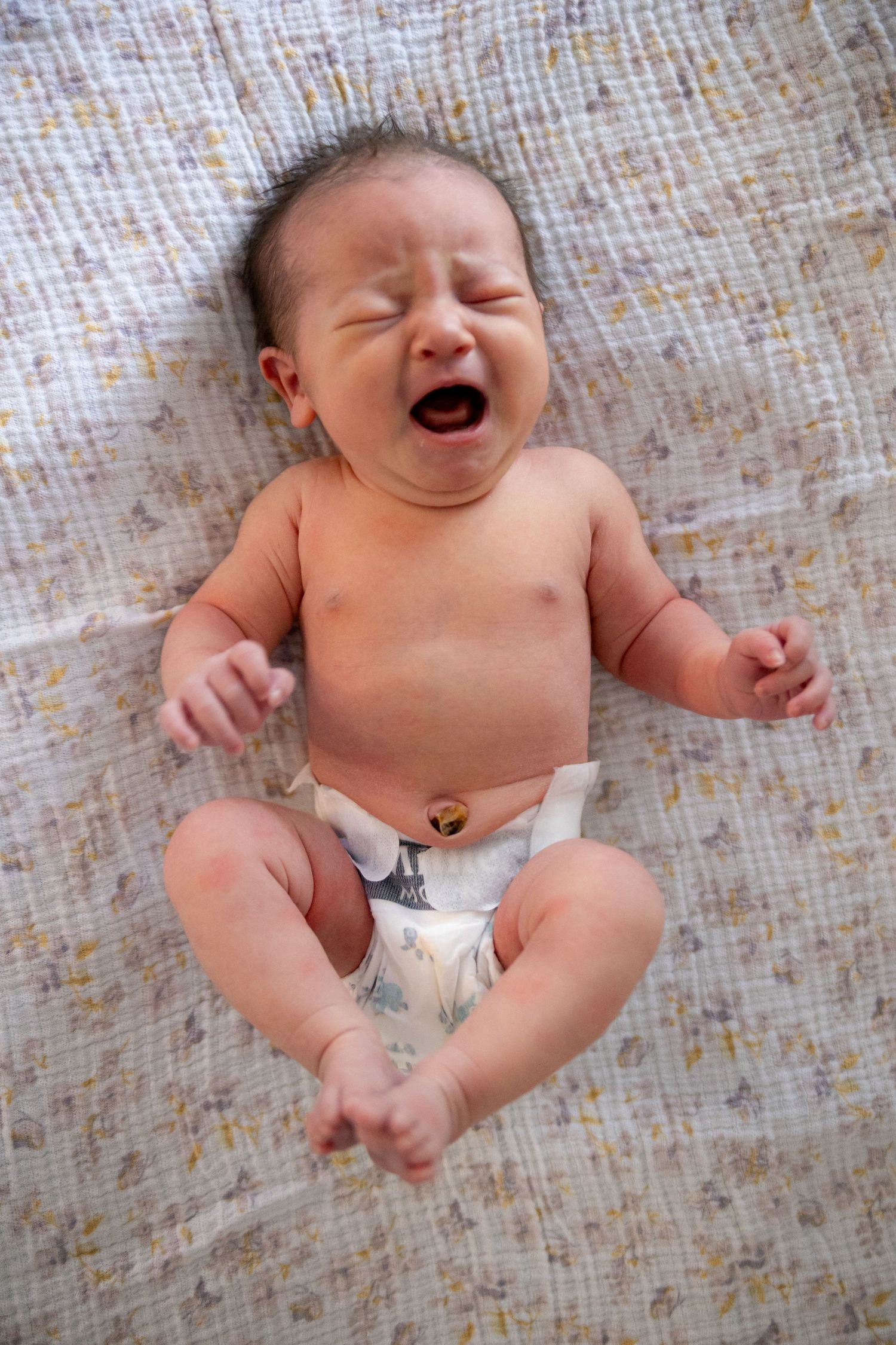 Happy laughing baby lying on floral pattern blanket wearing diaper.