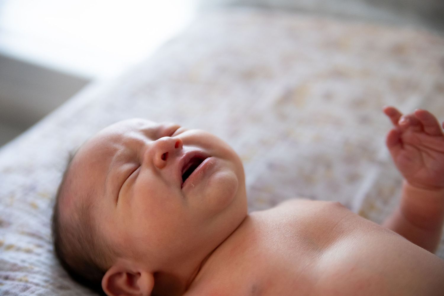 Happy laughing baby lying on blanket with eyes closed and hands raised.