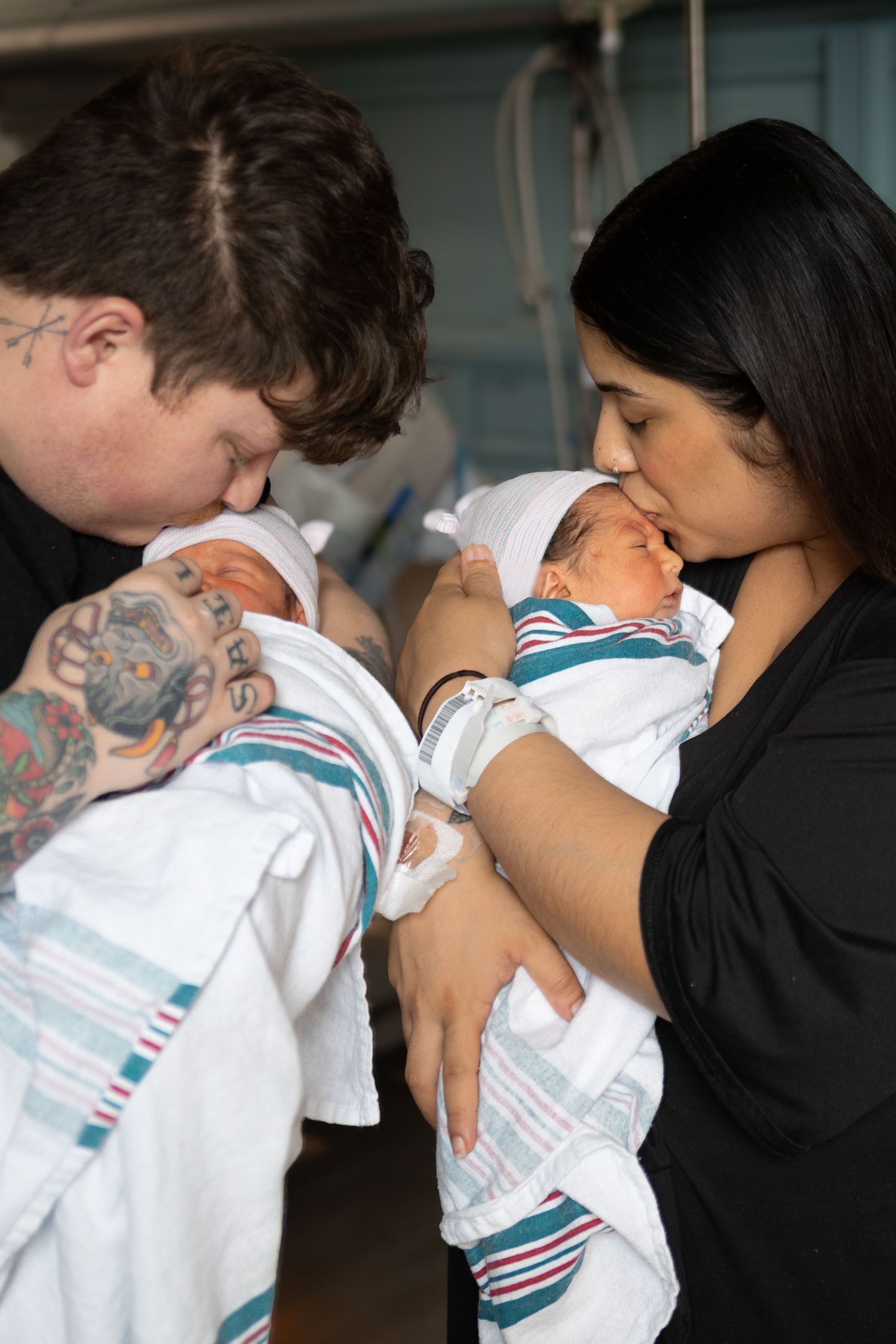 Two parents tenderly gaze at their newborn baby swaddled in a striped blanket in a hospital setting.