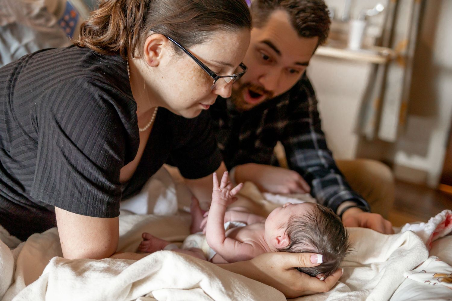 Parents share a tender moment with their newborn baby lying on white bedding.