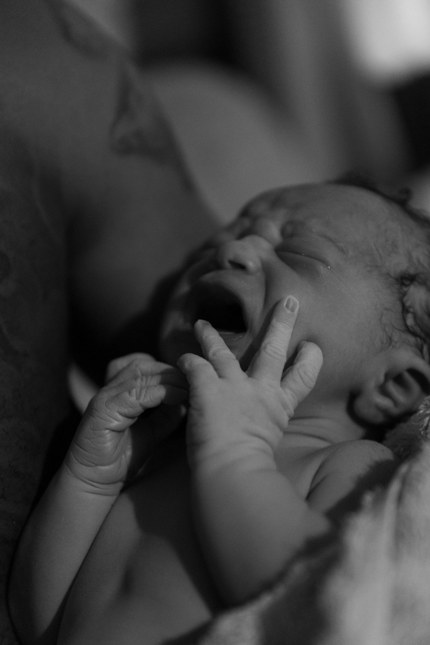 Black and white close-up images show a newborn baby's face and hands in a series of tender moments.