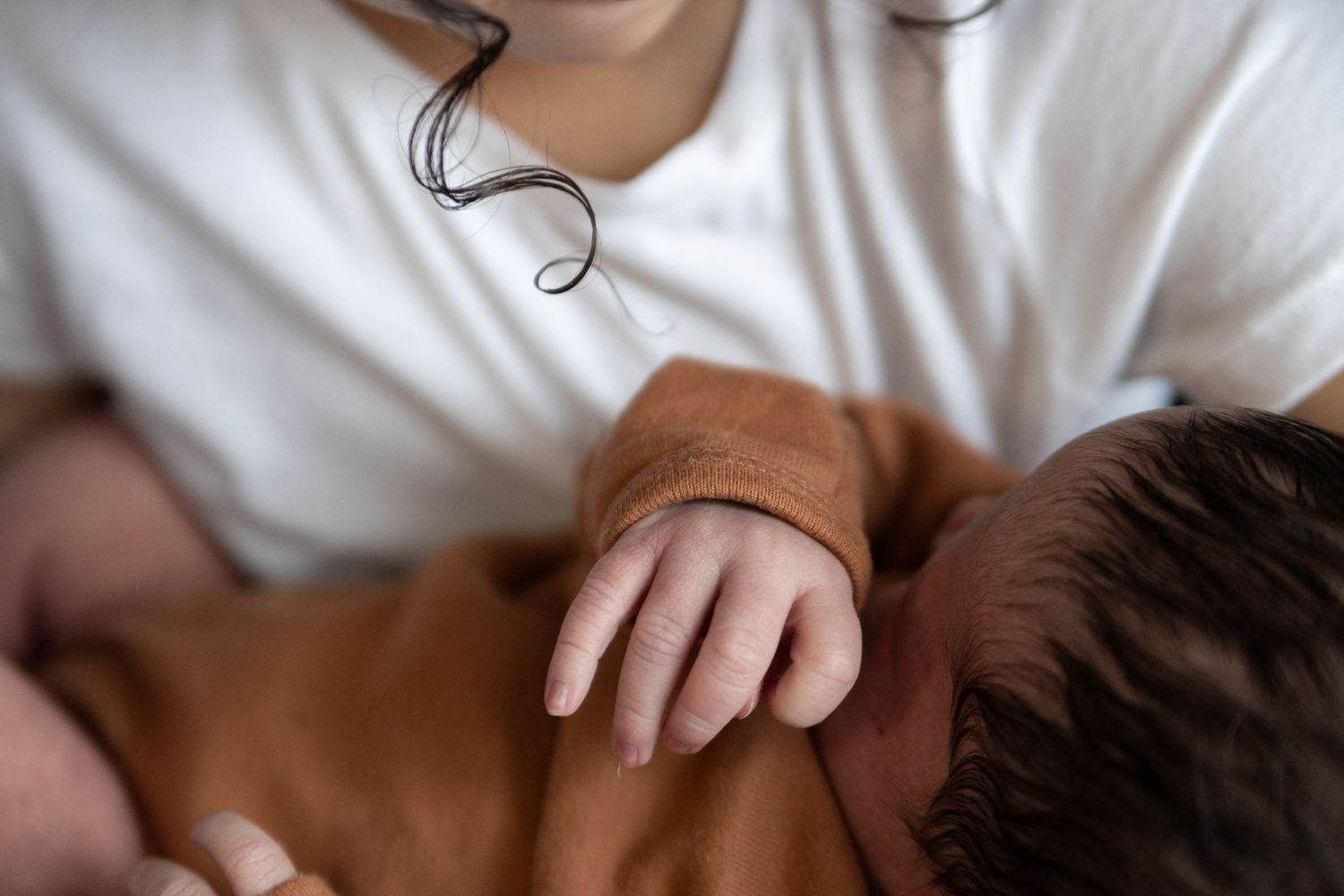 Close-up view of small hand resting against brown fabric while breastfeeding or nursing.