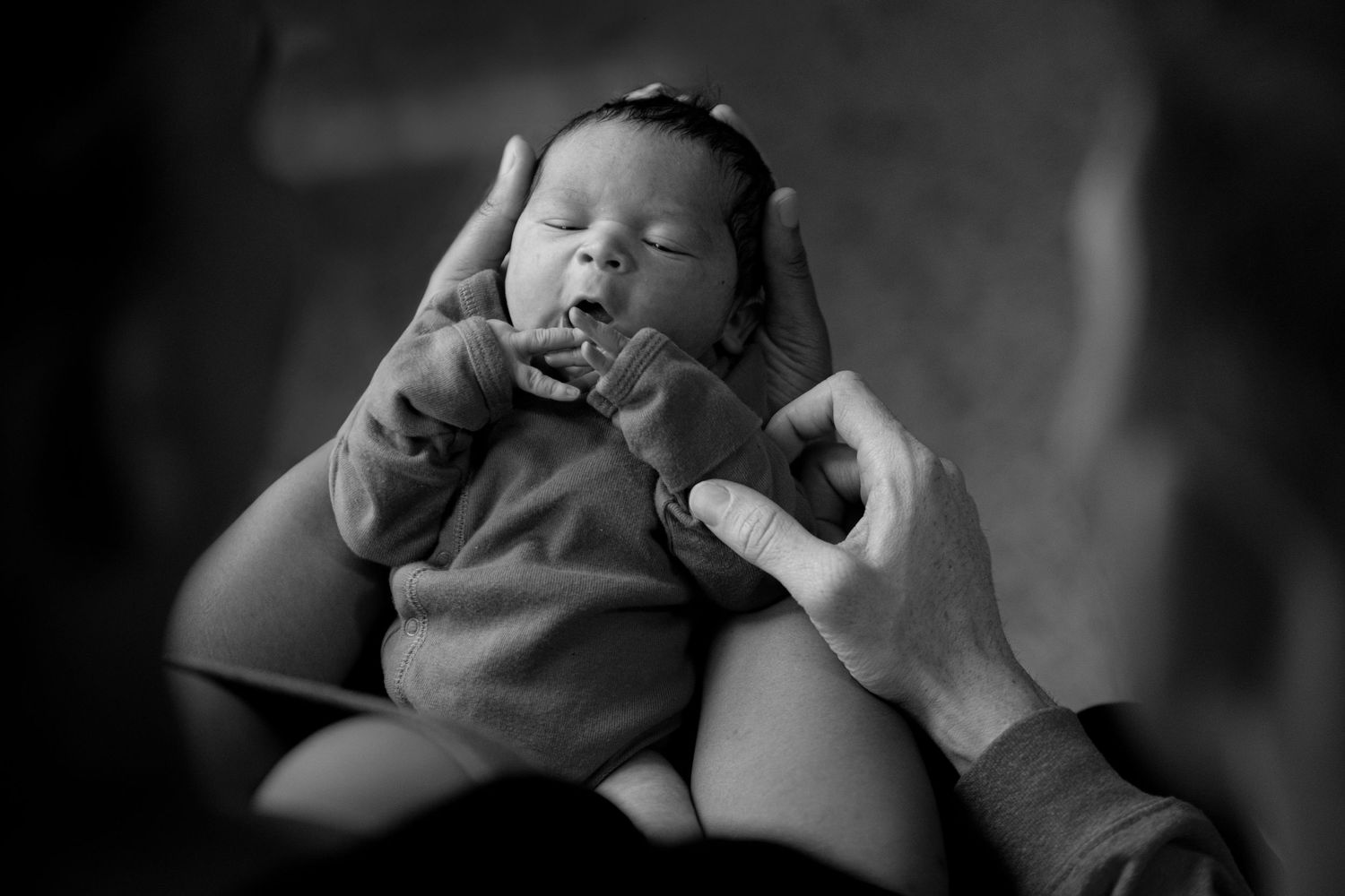 A tender black and white portrait of a newborn baby being gently held and comforted.