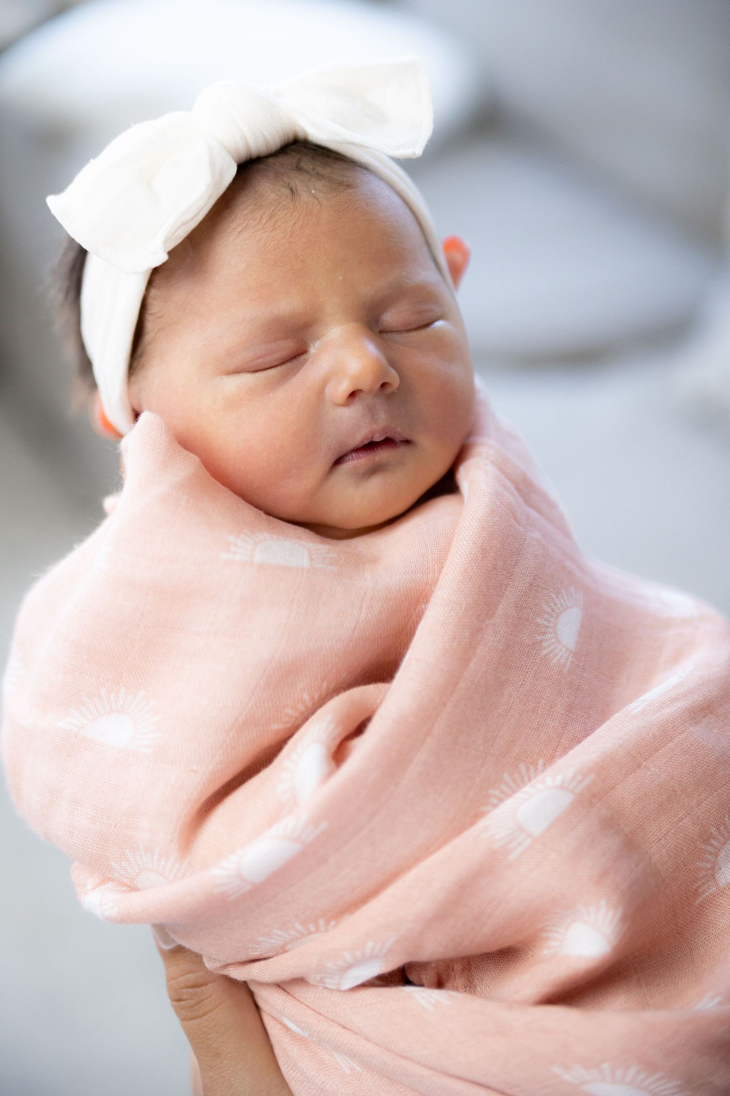 Sleeping newborn baby swaddled in pink blanket wearing white hat captured in multiple closeup shots.