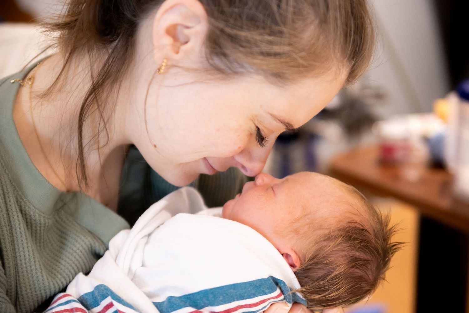 A tender moment captured as a woman in a green shirt gently leans over a swaddled baby.