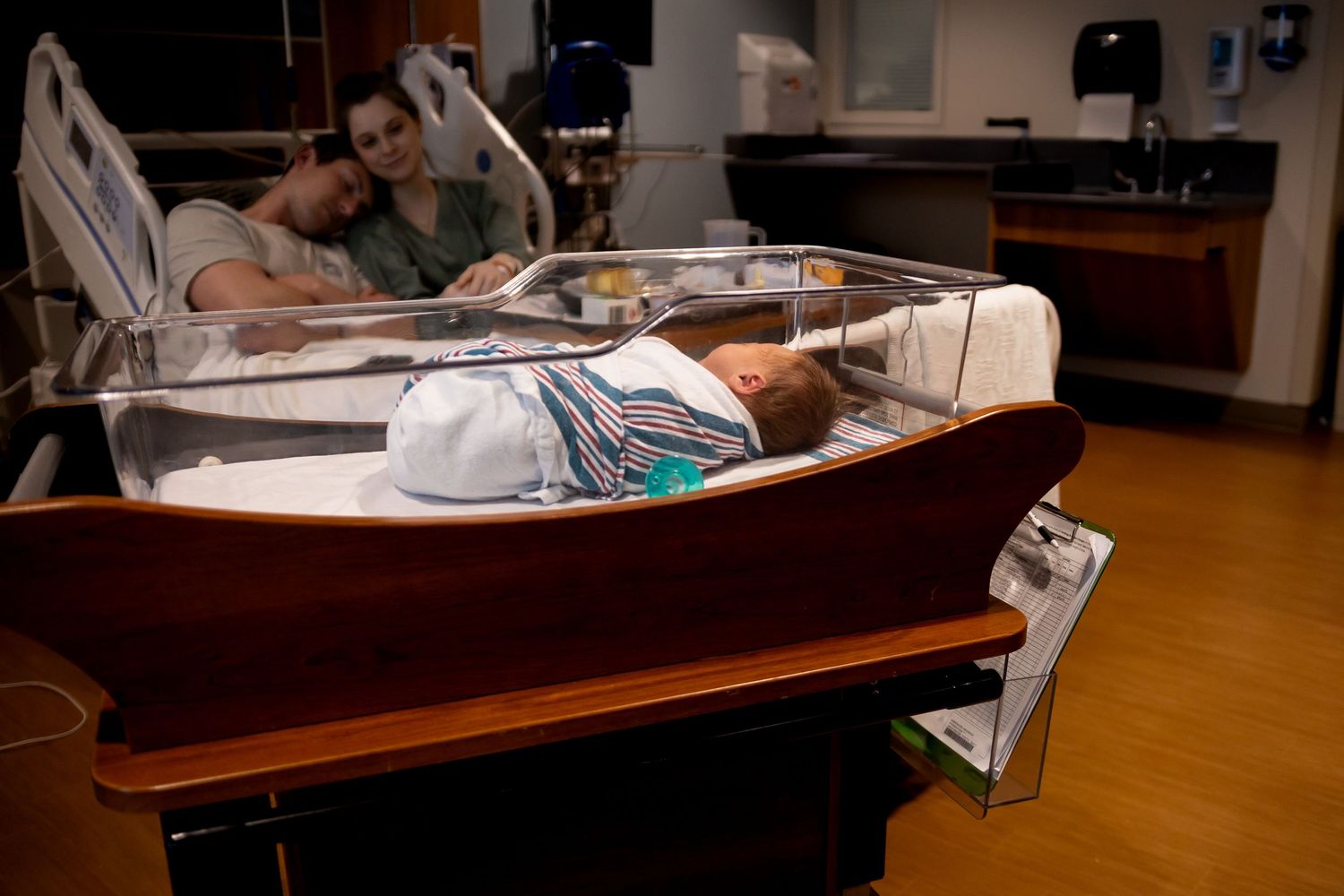 A newborn baby rests in a hospital bassinet with monitoring equipment in a medical facility.