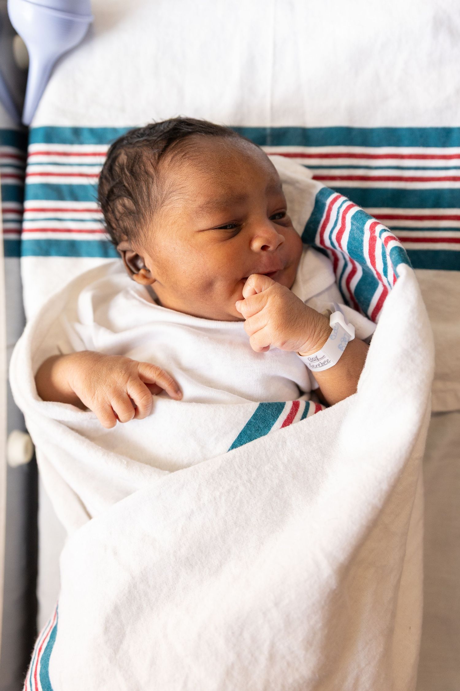 A sleeping newborn baby wrapped in a white blanket with teal and red striped trim.