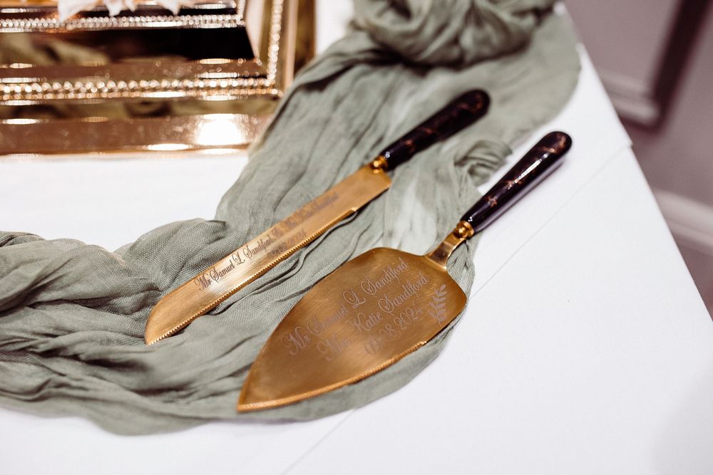 Personalized gold engraved wedding cake cutting set with knife and server on a gray silk ribbon.