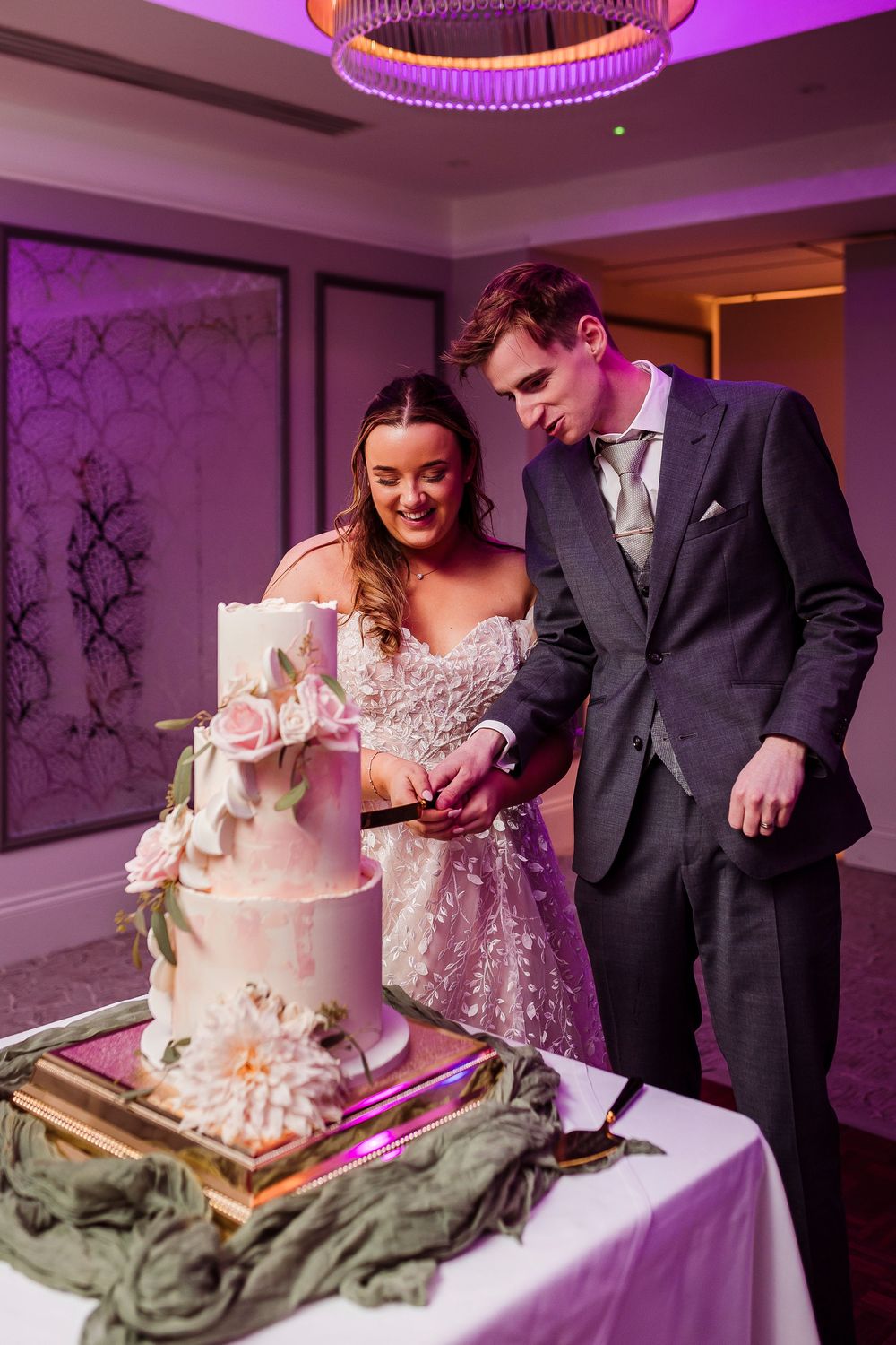Bride and groom cutting their elegant three-tier wedding cake decorated with pink roses at their wedding reception.