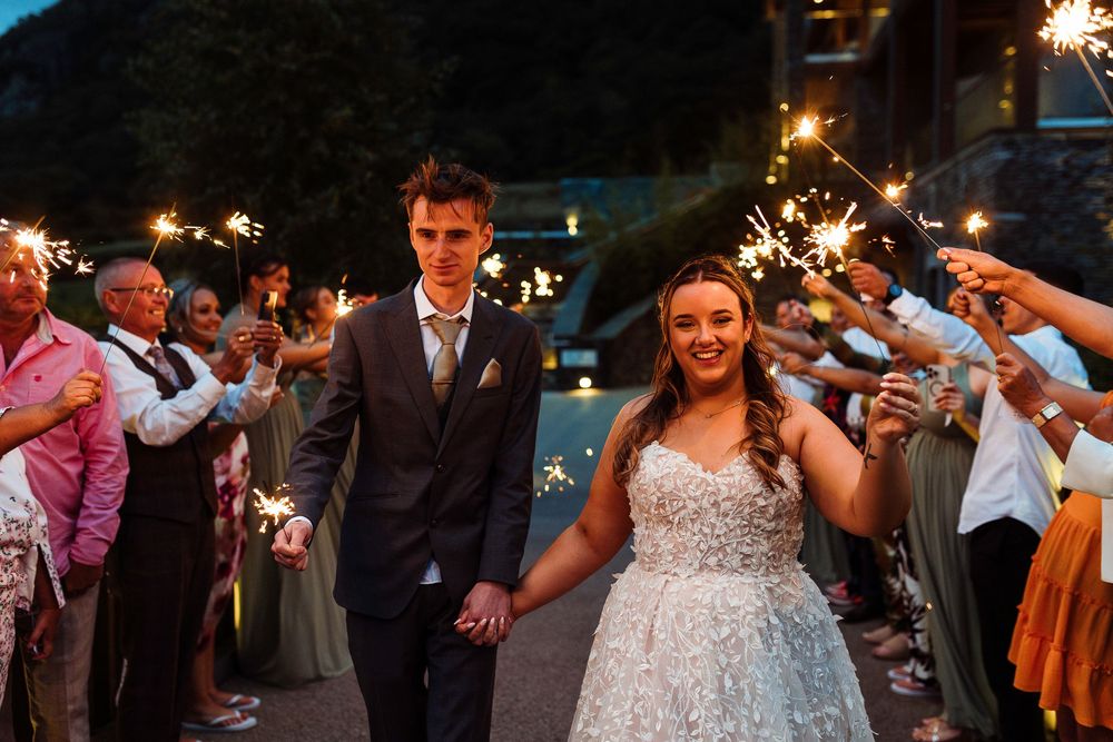 Bride and groom walk through sparkler tunnel surrounded by guests at elegant evening wedding celebration.