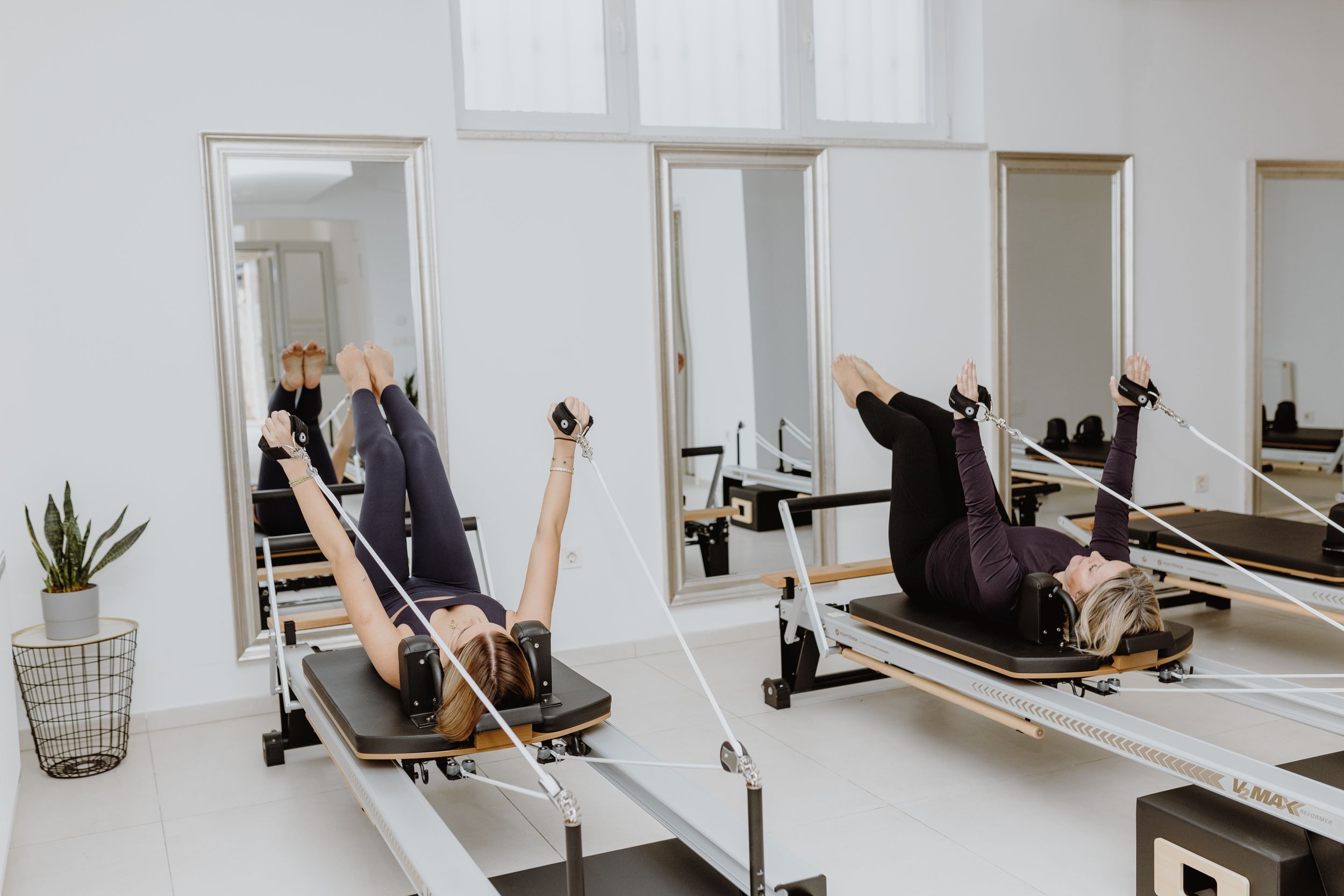Two women in action on Pilates reformer machines, shown in brand photography that emphasizes their strength.