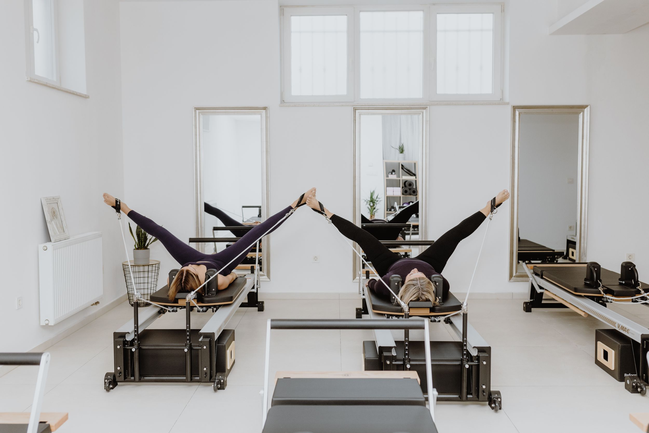 Brand fotografija dviju žena koje izvode Pilates vježbe na reformerima u moderno opremljenom studiju u Zagrebu.