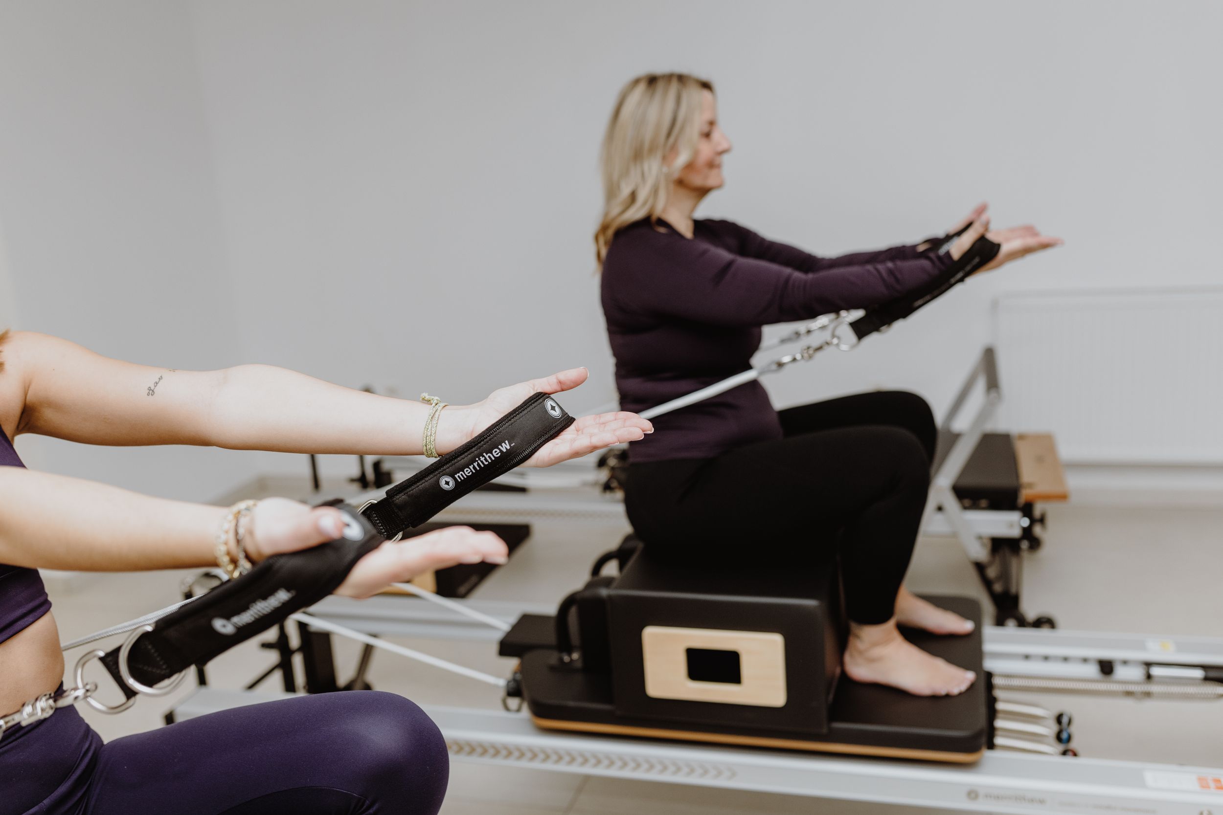 People exercising on Pilates reformer machines in a bright studio.