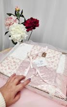 Pink floral gift set in elegant packaging with satin ribbon, accompanied by fresh pink and red peonies on a white background.