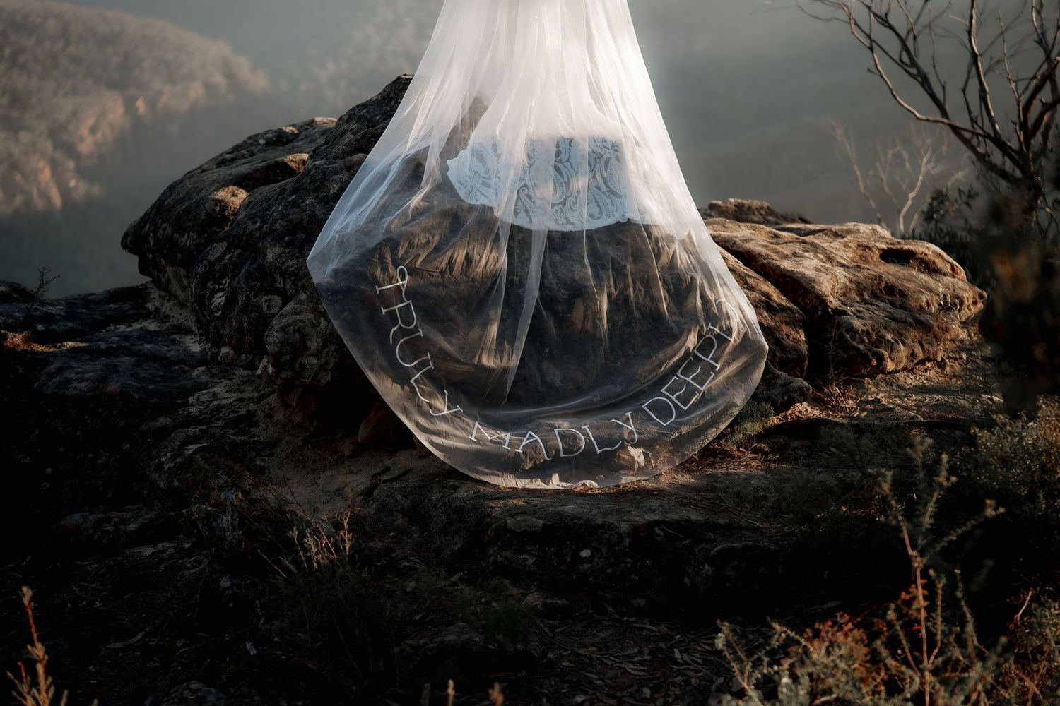 A translucent plastic bag with text rests on rocky terrain with misty mountains in the background.