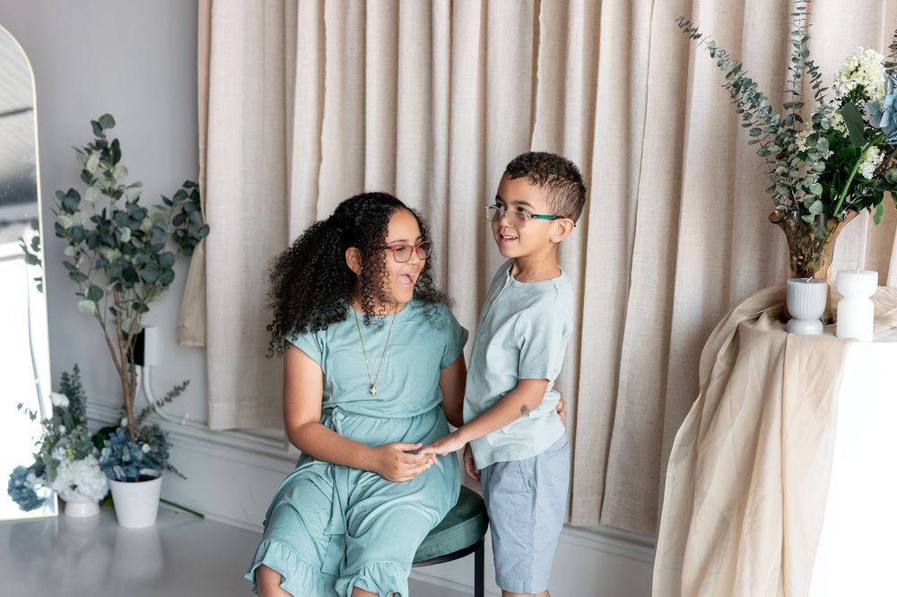 Two siblings in matching teal outfits share a sweet moment together in a softly decorated indoor setting.