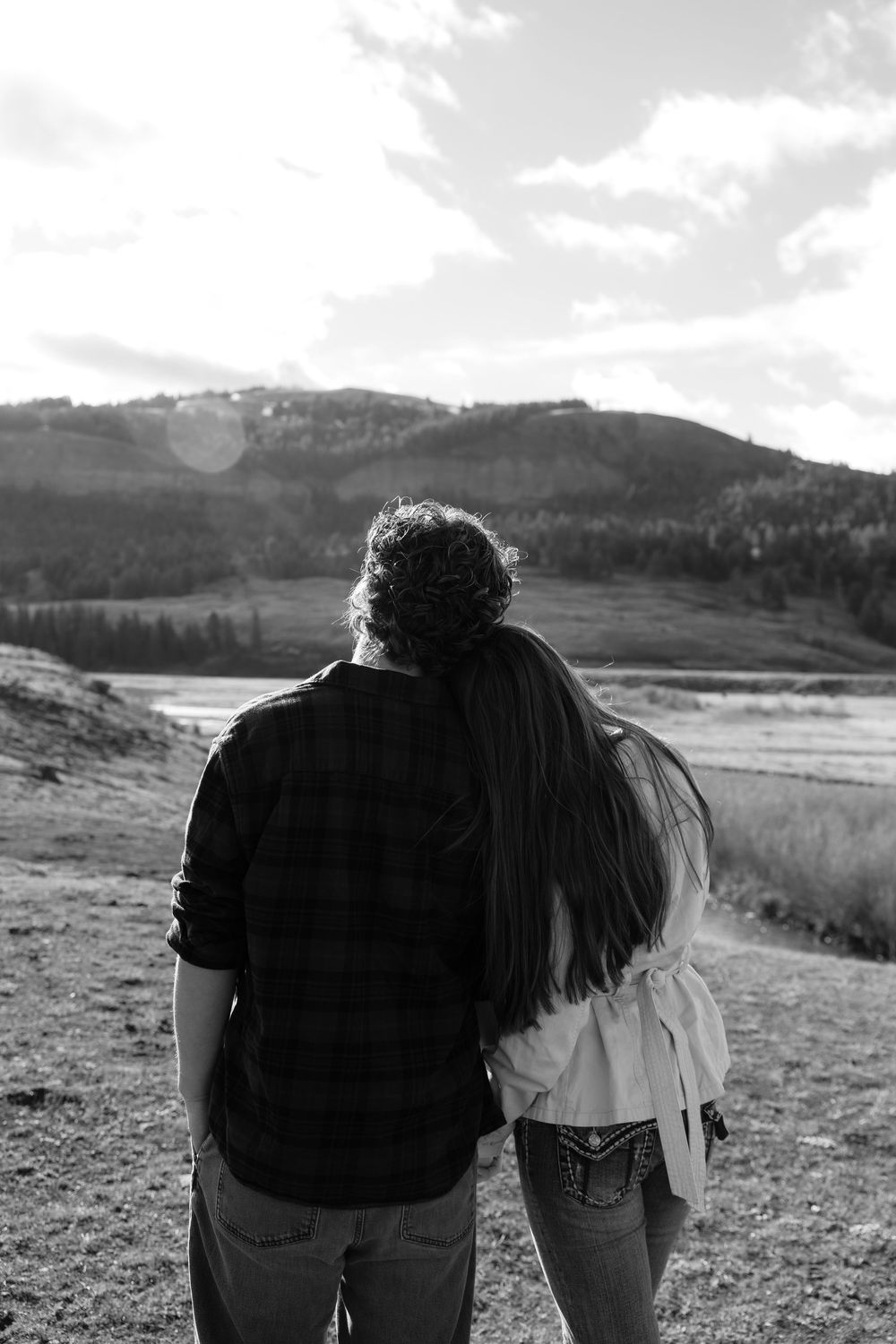 Black and white photo of couple standing together gazing at a mountain valley landscape.