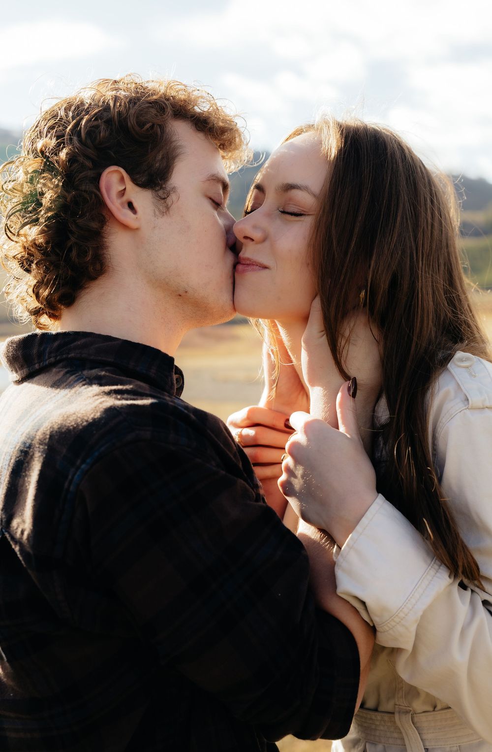 A romantic young couple shares a kiss outdoors in a scenic natural landscape on a sunny day.