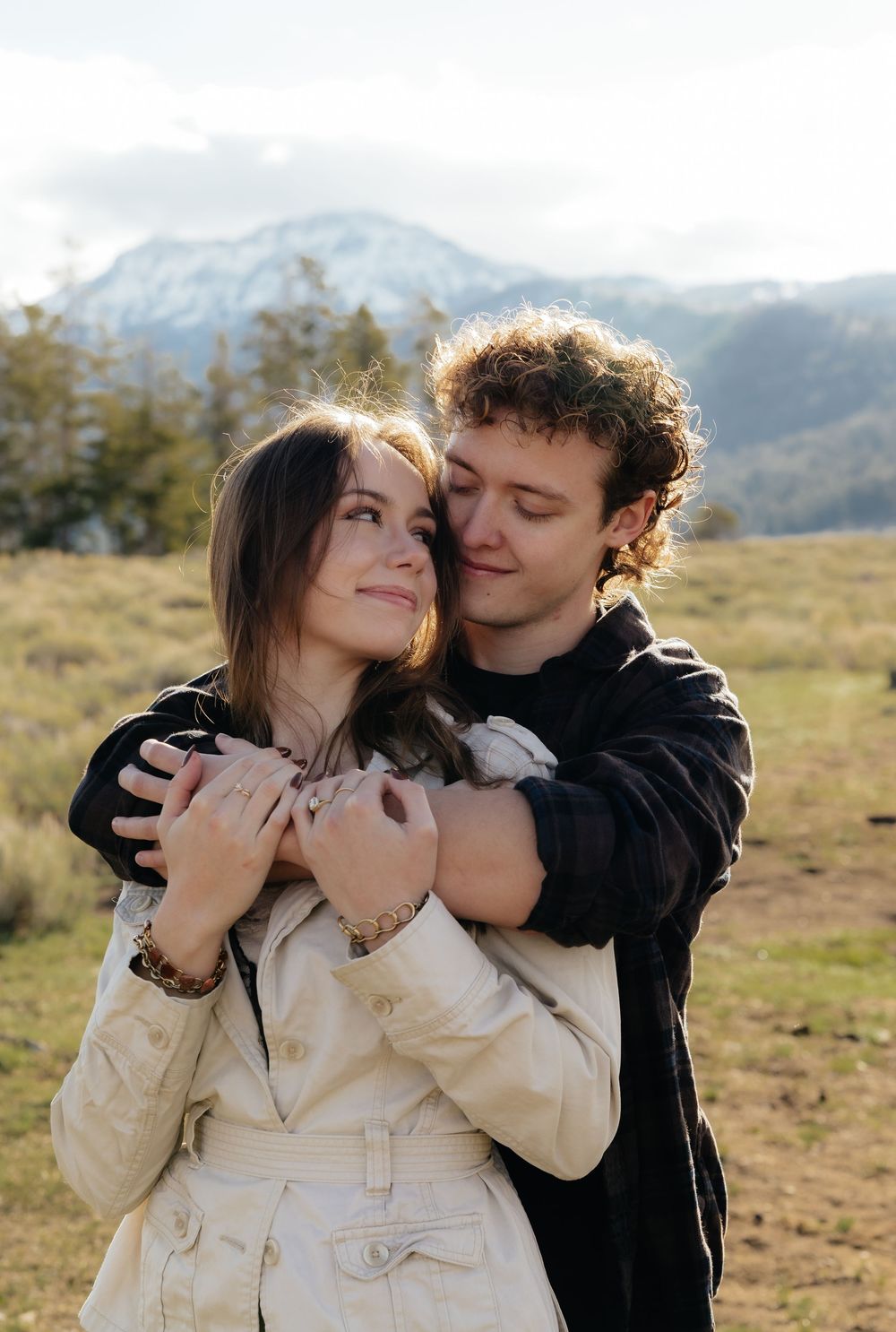 A happy couple shares a tender embrace with snow-capped mountains visible in the background.