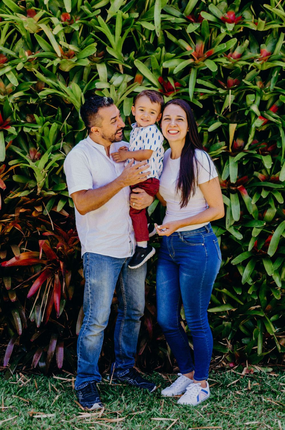 Family poses together in front of lush tropical plants with vibrant red flowers.