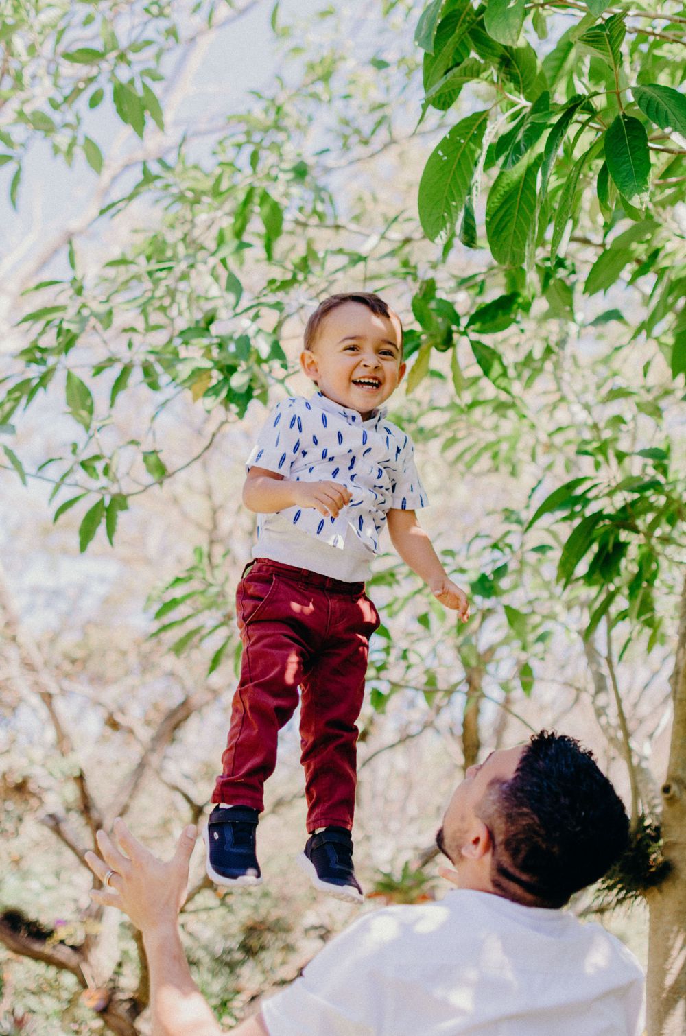 A joyful moment captured mid-air against green foliage on a sunny day.