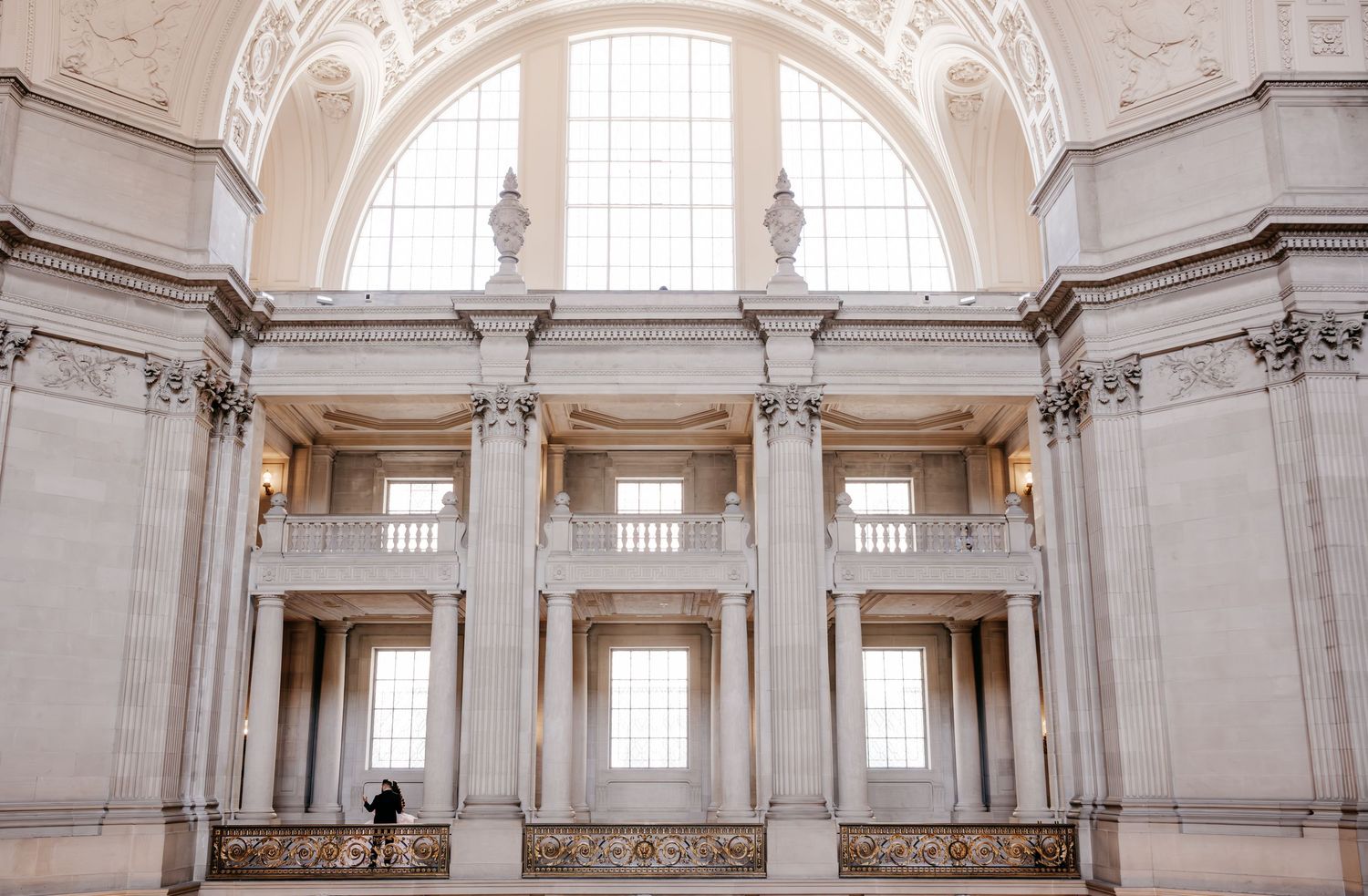 Grand neoclassical interior of San Francisco City Hall rotunda with marble columns and arched windows.