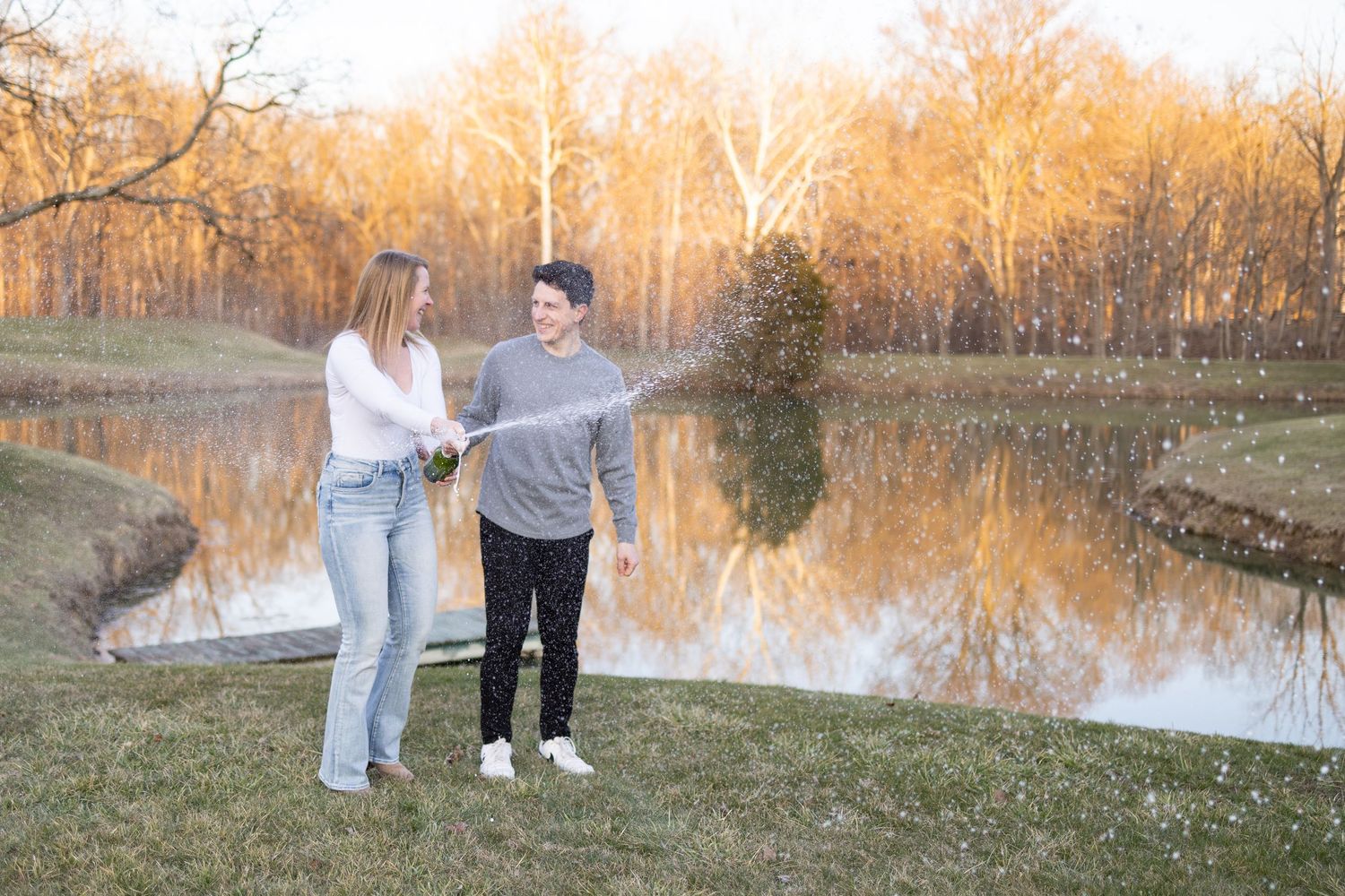 Couple holding hands by a reflective pond surrounded by autumn trees at golden hour.