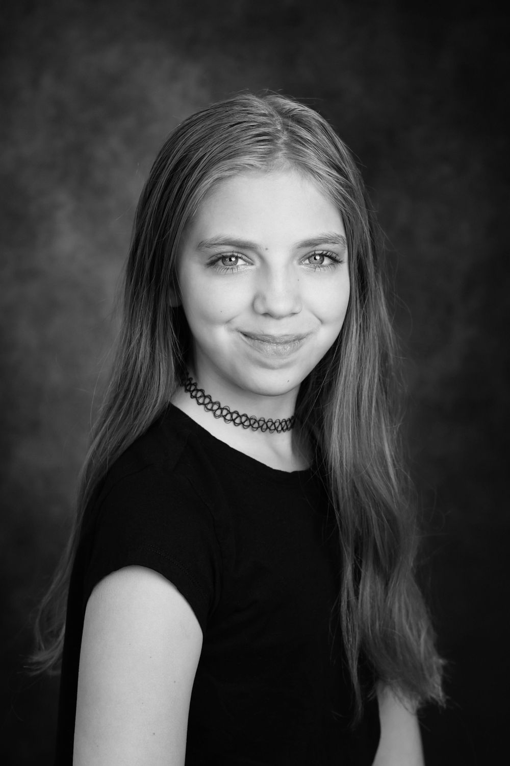 Black and white portrait of a teenage girl with long hair wearing a black top and choker necklace.
