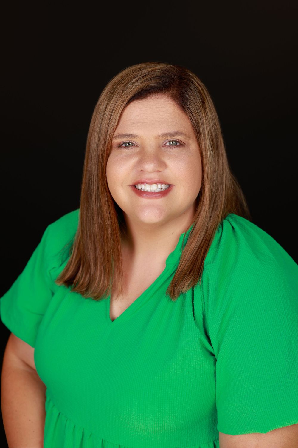 Professional headshot of a smiling woman with brown hair wearing a bright green v-neck top.
