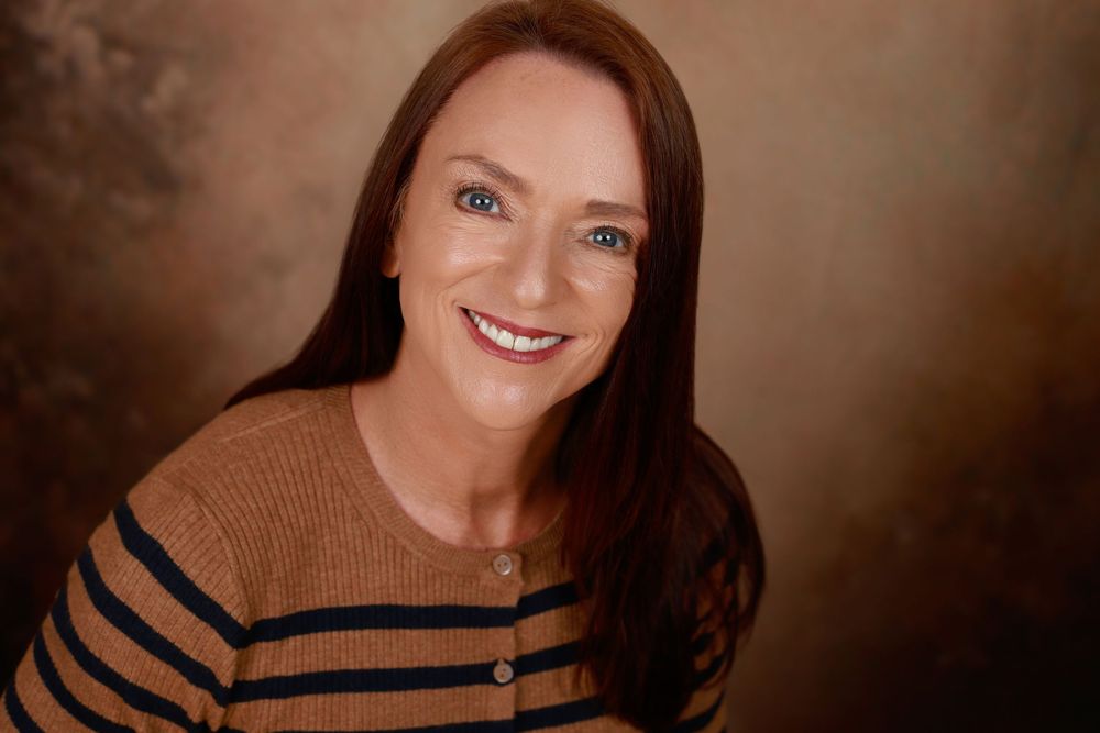 Smiling woman with auburn hair wearing a striped brown sweater in a professional headshot.