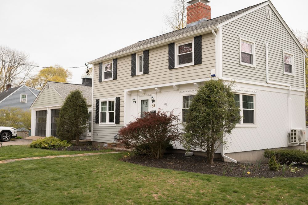 Traditional colonial-style home with gray siding, black shutters, and landscaped front yard.